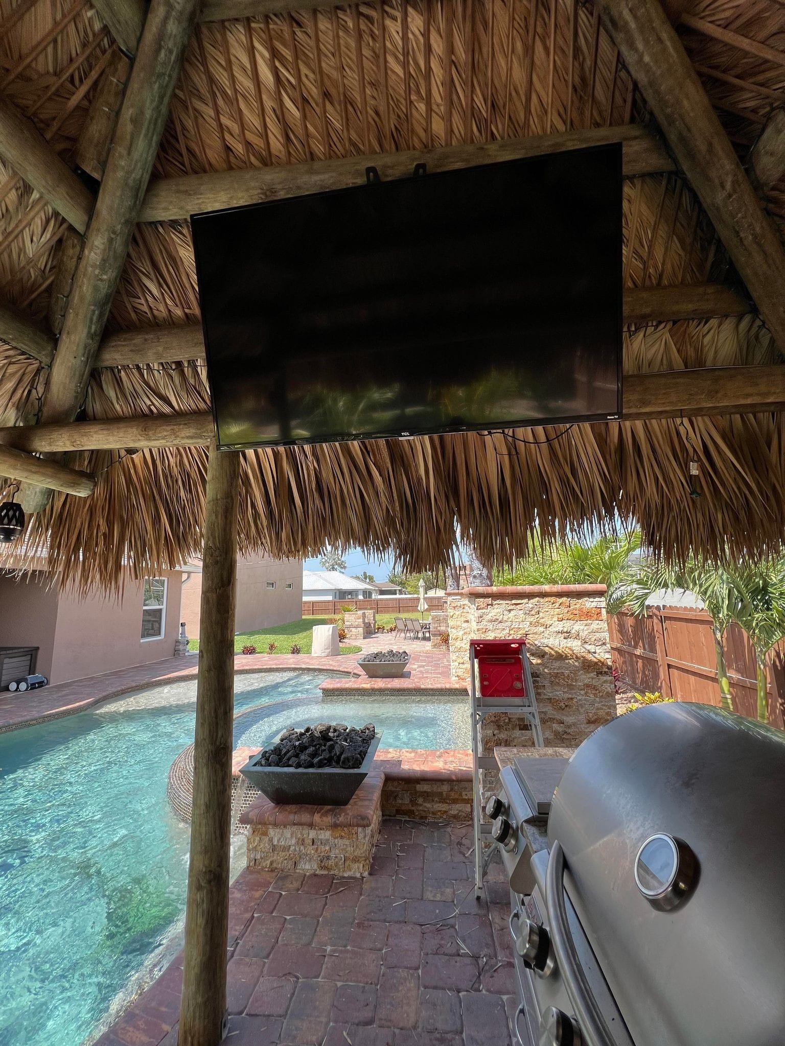 Tiki with tv and grill next to a pool